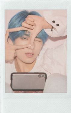 a man with blue hair holding his hands up to his face while looking at a cell phone