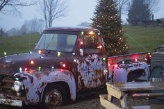 an old rusty truck with christmas lights on the hood parked in front of a tree