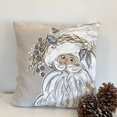 a decorative pillow with an image of a santa clause on it next to a pine cone