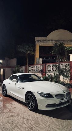 a white bmw z4 parked in front of a house at night with its lights on