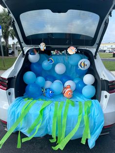 the trunk of a car with balloons in it and fish decorations on the tailgate