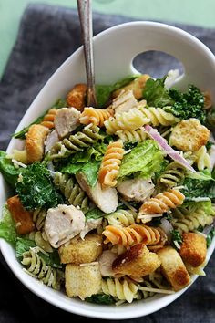 a white bowl filled with pasta salad on top of a blue napkin and silver spoon