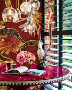 a table with flowers and books on it in front of a wallpapered window