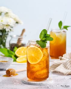 two glasses filled with iced tea and lemons on a table next to some flowers