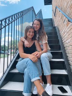 two young women sitting on the steps of a brick building, one with her arm around the other's shoulder