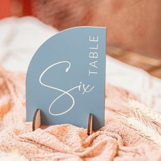 a blue table sign sitting on top of a bed next to a pile of blankets