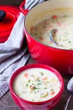 a red pot filled with soup next to a bowl full of soup and spoons