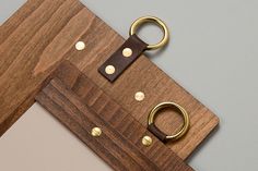 a wooden cutting board with two brass rings on it and a leather keychain