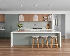 a kitchen with wooden flooring and white counter tops next to two stools in front of an island