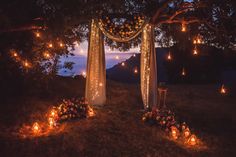 an outdoor wedding setup with candles and flowers on the ground at night time, surrounded by trees