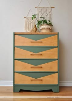 a green and wood dresser with some plants on it's top, in front of a white wall