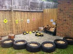 there are many tires on the ground in front of a fence and some barrels full of wood