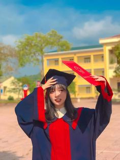 a woman wearing a graduation cap and gown holding up a red ribbon in front of her head