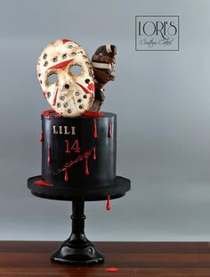 there is a cake decorated with a mask and blood dripping down the side, on top of a wooden table