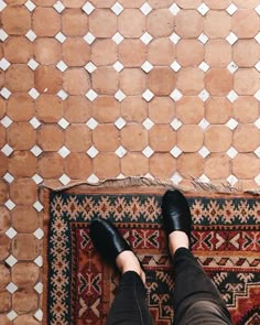 a person wearing black shoes standing in front of a rug