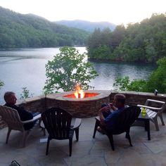 two men sitting around a fire pit on top of a stone patio next to a lake