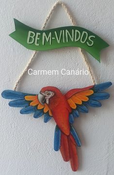 a colorful bird hanging from the side of a wall next to a sign that says bem - vindos