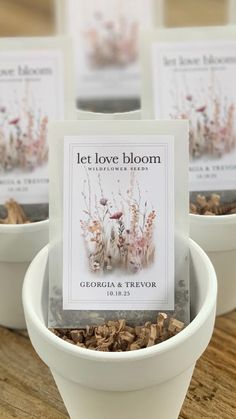 three small white bowls filled with flowers on top of a wooden table next to cards that say let love bloom