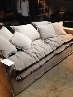 a couch with many pillows on it in front of a man standing next to the couch