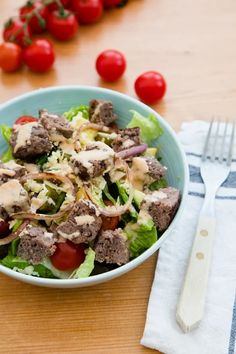 a salad with meat, tomatoes and dressing in a blue bowl on a wooden table