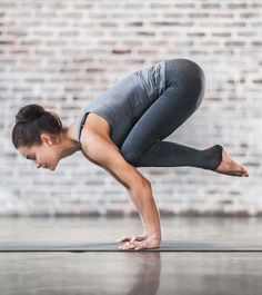 a woman is doing yoga in front of a brick wall with her hands on the ground