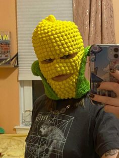 a person taking a selfie with a cell phone in front of them wearing a yellow crocheted head