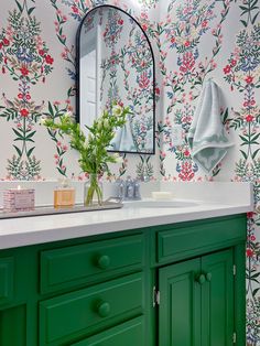 a bathroom with green cabinetry and floral wallpaper on the walls, along with a large mirror