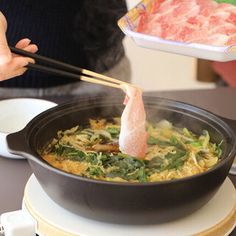 a person holding chopsticks over a skillet filled with food