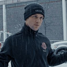 a man standing in the snow wearing a black jacket and hat with his hands out