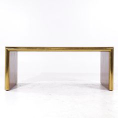 a gold and grey rectangular table on a white floor with an empty wall in the background