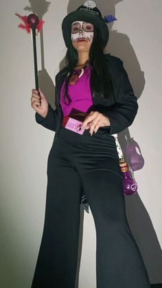 a woman in black pants and pink shirt holding a stick with white paint on her face