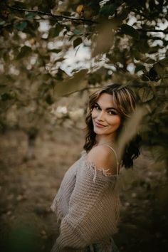 a woman standing under a tree with her eyes closed and looking at the camera while wearing a sweater