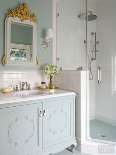 a white bathroom with blue and gold decor on the vanity, shower stall and sink