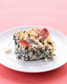 a white plate topped with pasta and spinach covered in cheese, sauce and bacon