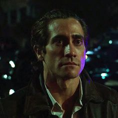 a man in a leather jacket looking off into the distance with city lights behind him