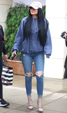 a woman with long black hair wearing ripped jeans and a blue hoodie is walking down the street