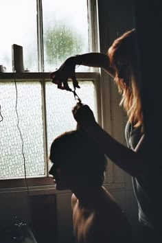 a woman blow drying her hair in front of a window