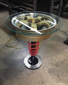 a round glass table with red springs on the bottom and metal base, in an industrial setting