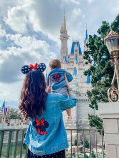 a woman holding a child in front of a castle at disney world with the castle behind her