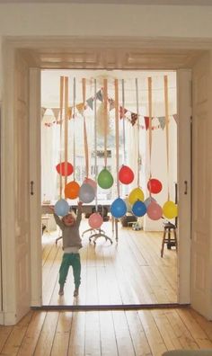 a young boy standing in front of an open door with balloons on the wall behind him