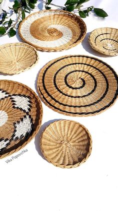 four woven baskets sitting on top of a white surface next to green leaves and flowers