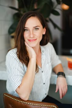 a woman sitting at a table with her hand on her chin and looking into the camera