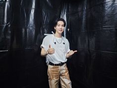 a young man standing in front of a black backdrop giving the thumbs up sign with both hands