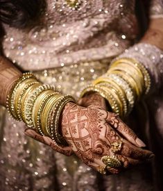 a woman wearing gold bracelets and holding her hands with hennap on it