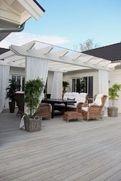 an outdoor living area with white curtains and wicker furniture on the wooden flooring