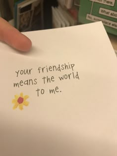 a hand holding a piece of paper that says your friend means the world to me