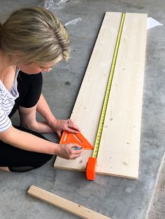 a woman sitting on the floor working on some wooden planks with a measuring tape