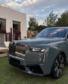 a grey rolls royce parked in front of a house with grass and trees around it