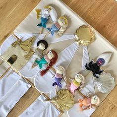 an assortment of little mermaids on top of a white table cloth with gold trim