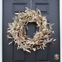 a wreath hanging on the front door of a house that is decorated with dried leaves